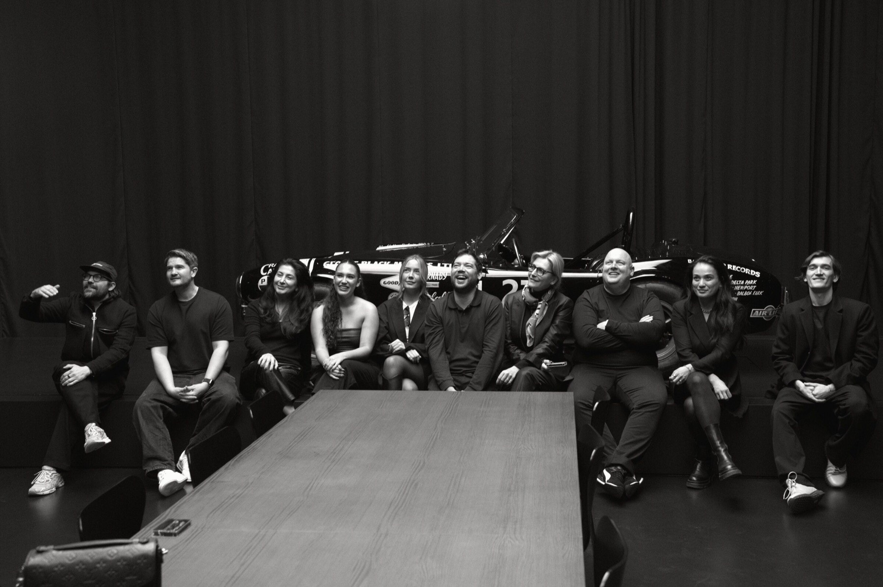 The ten dinner guests seated together in front of the race car.