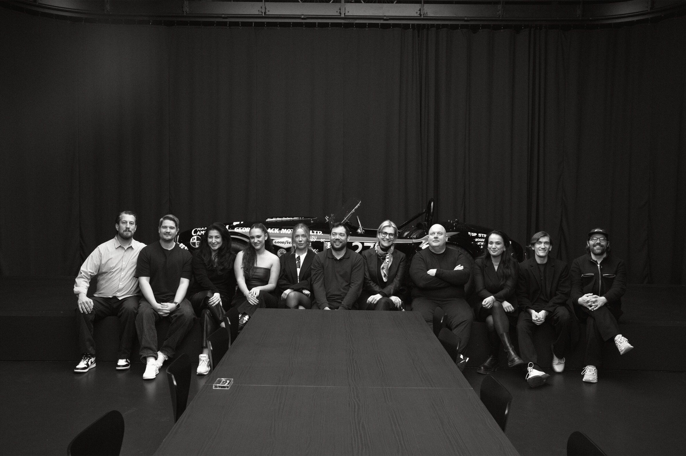 The ten guests seated together in front of a historic race car after dinner.