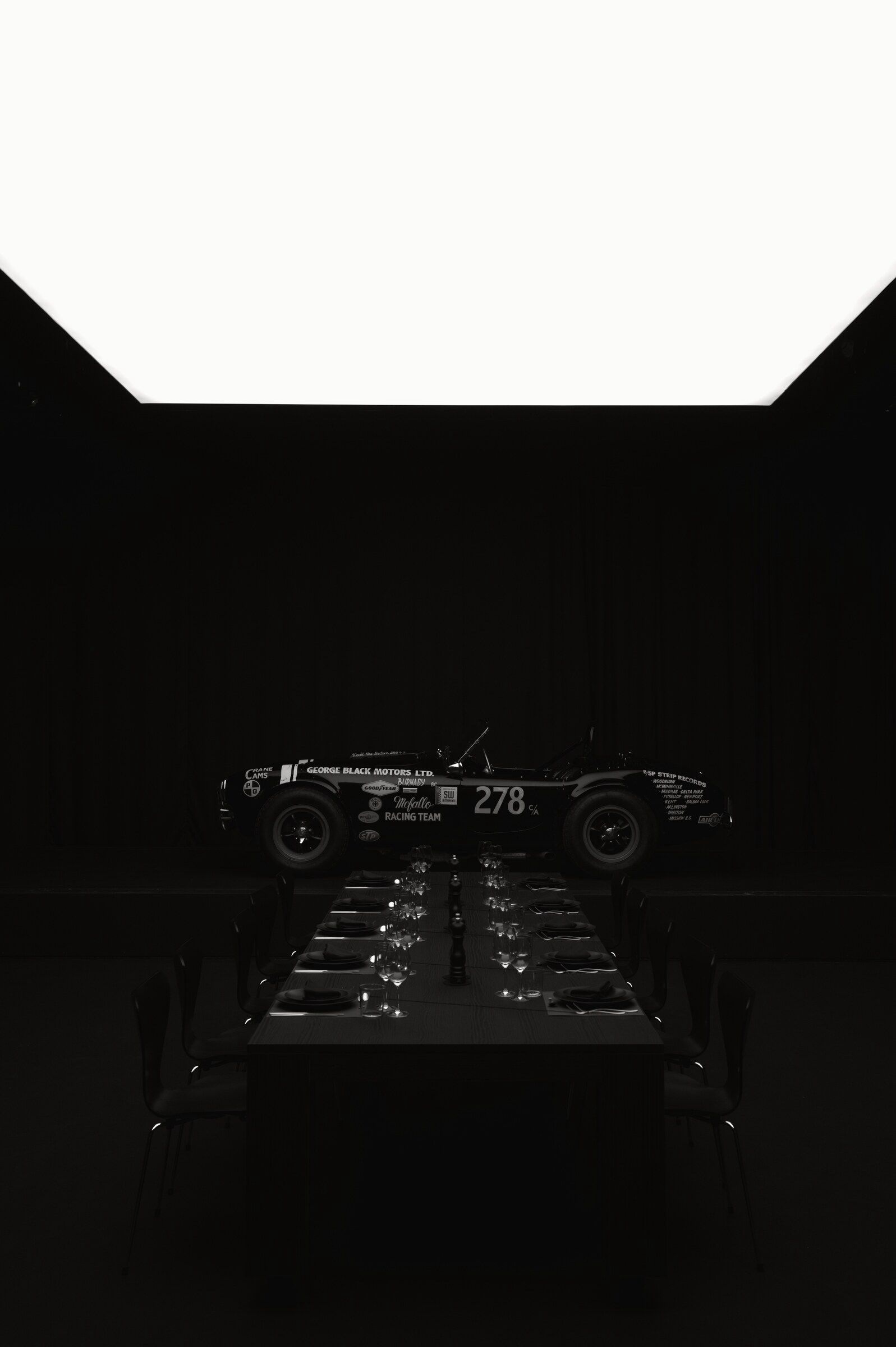 A table set for ten with a historic racing car at the far end of a dark automotive space.